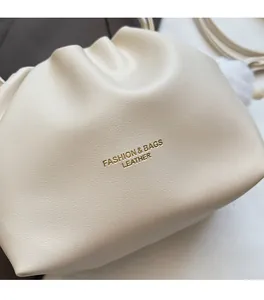 Detail of cream pleated bucket bag with gold lettering and white fur pom-pom charm