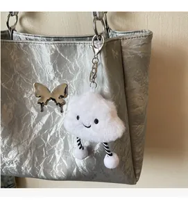 Detail of a white plush cloud charm with striped legs hanging on a silver tote bag