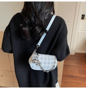Détail du sac à bandoulière à carreaux bleus avec chaîne argentée porté par un modèle