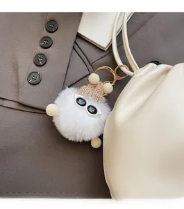 Detail of white plush charm with mini knit hat and sunglasses on leather handbag