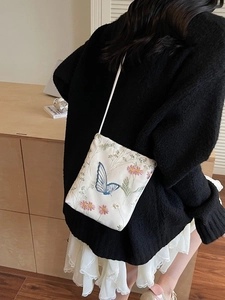 Sac seau blanc minimaliste avec broderie papillon et bandoulière porté par un mannequin