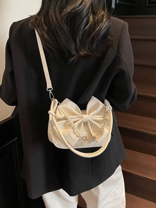 White bow-shaped crossbody bag with pearl chain and pleated fabric on a model