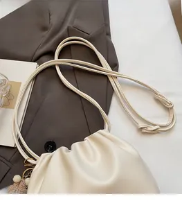 Close-up of cream pleated cloud bag with pom-pom charm and slim double straps