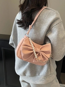 Pink shoulder bag with large bow and pearl chain strap worn by model in casual style