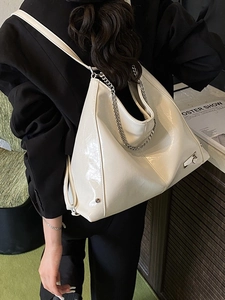 Glossy cream leather tote bag with silver chain strap shown on a model in a black suit