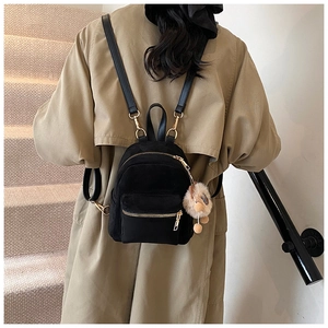 Detail of mini black quilted backpack with plush charm on stylish model in trench coat