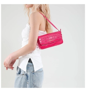 Detail of fuchsia crocodile texture bag with gold metal logo and sleek shoulder strap