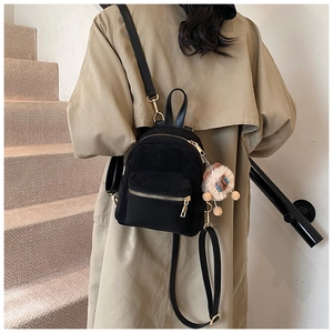 Detail of black mini backpack with golden zippers and a cute plush toy charm