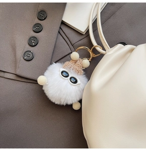 Detail of cute white plush ball charm with sunglasses and mini knit hat on a leather bag