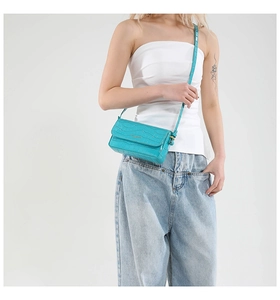 Detail of cyan blue faux crocodile leather shoulder bag with gold logo on white background
