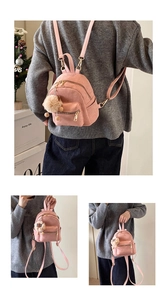 Detail of pink mini backpack with fuzzy charm and gold zippers on soft matte texture
