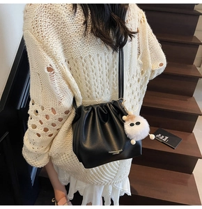 Detail of black pleated bucket bag with leather texture and cute plush monster charm
