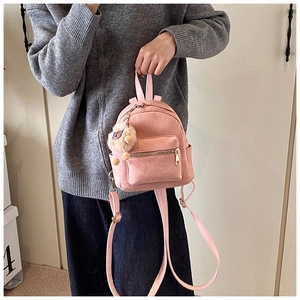 Detail view of mini pink suede backpack with a fluffy pom-pom charm and metal zipper