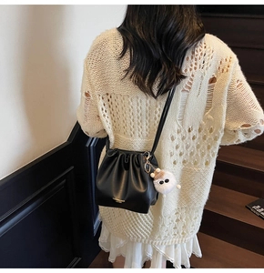 Detail of black leather bucket bag with drawstring and cute white pom-pom charm decoration