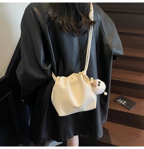 Detail of a creamy white drawstring cloud bag with fashion text and a plush doll pendant