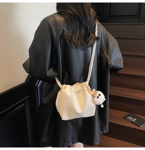Detail of off-white drawstring bucket bag with plush charm on a model back view