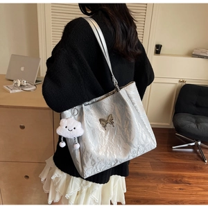 Detail of silver tote bag with butterfly ornament and plush cloud charm on shoulder strap
