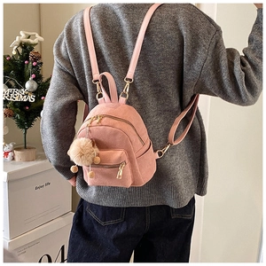 Close-up of pink frosted leather backpack featuring a beige pompom charm and gold zippers