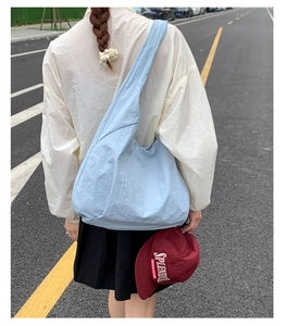 Detailed back view of a light blue nylon tote bag with wide straps in a street setting