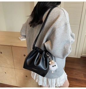 Detail of black leather bucket bag with drawstring folds and cute white plush doll charm