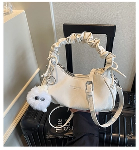 Détail du sac croissant plissé blanc cassé avec peluche sur une valise noire