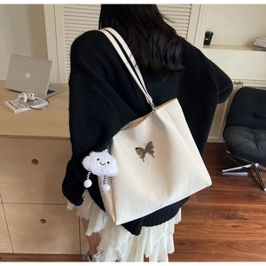 Detail of cream tote bag with butterfly buckle, cloud charm, and laptop setup