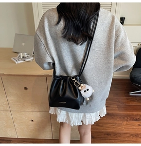 Detail of black leather drawstring bucket bag with a cute plush charm and shoulder strap