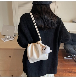 Close-up of cream pleated cloud bag with plush charm and fashion logo detail
