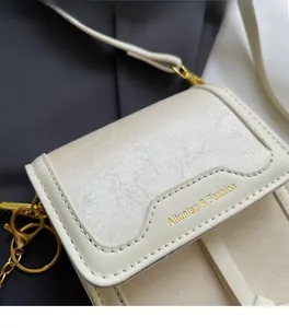 Detail der cremefarbenen Umhängetasche aus Leder mit goldener Logo-Prägung auf Anzugstoff
