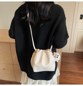 Creamy white drawstring bucket bag detail with plush charm and fashion logo text