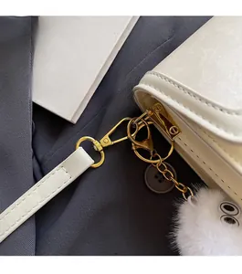 Detailansicht der cremefarbenen Ledertasche mit goldener Hardware und Plüsch-Anhänger