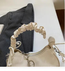 Détail d'un sac à main beige avec poignée plissée, fermeture argentée et lettrage