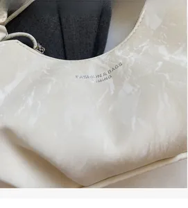 Détail de la texture en cuir plissé beige et du logo argenté sur le côté du sac à main