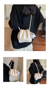 Detail view of cream pleated drawstring bucket bag with a plush pompom and strap