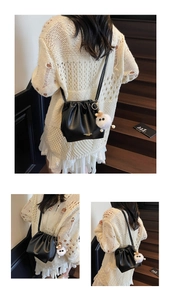 Detail view of a black pleated bucket bag with a white plush charm and sleek strap