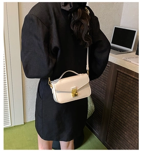 Detail of a chic cream crossbody bag with gold metal lock and leather shoulder strap