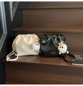 Detailed view of drawstring bucket bags in beige and black leather with plush charms