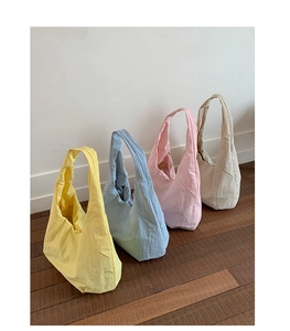 Minimalist large nylon tote bags in yellow, blue, pink, and white on a wooden floor