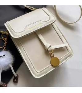 Detailansicht der cremefarbenen Umhängetasche mit Goldlogo und flauschigem Monster-Anhänger