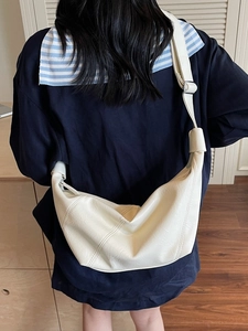 Minimalist cream crescent shoulder bag in soft leather texture worn by a model