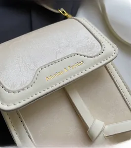 Detail der cremeweißen geprägten Leder-Umhängetasche mit feiner Naht und Goldlogo