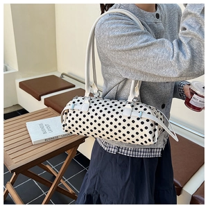 Detail van een witte bucket bag met zwarte stippen getoond op een model in een buitenomgeving
