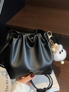 Chic black pleated bucket bag with plush charm and fashion branding in a lifestyle setting