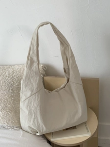 Minimalist beige oversized nylon tote bag with crinkled texture on wooden table