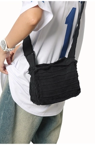 Detail of black denim crossbody bag featuring layered raw fringe and adjustable strap