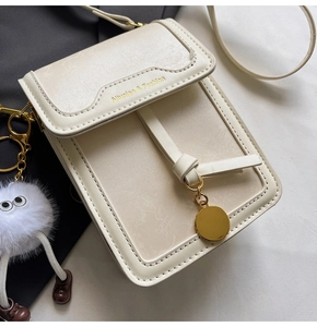 Detail einer cremeweißen Handytasche mit goldenem Logo und weißem Plüsch-Anhänger-Dekor