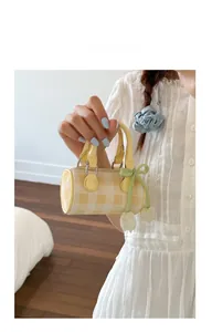 Detail of cream and white checkered cylinder handbag with a green bow charm