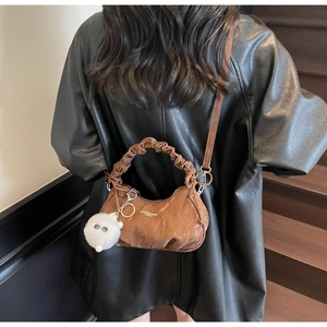 Détail d'un sac à main plissé marron avec charm en peluche et bandoulière amovible