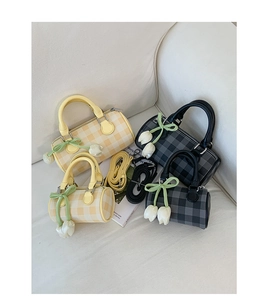 Detail of plaid boston bag with tulip pendant and green ribbon on white fabric