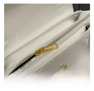 Close-up of golden zipper and hardware on white patent leather shoulder bag